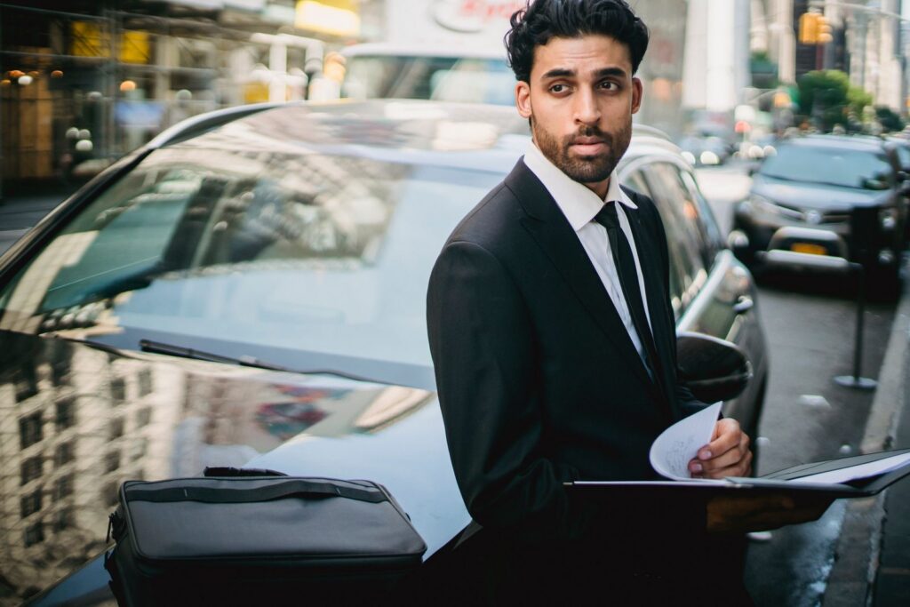 Man in a black suit leaning on a car, Highland Park airport limo service
